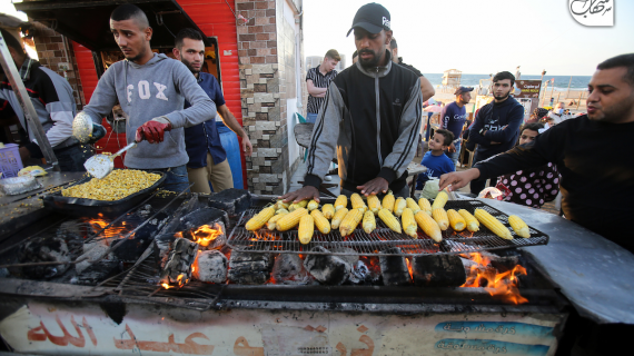 يقلبونها في وعاء معدني فوق موقد مشتعل.. بائعون على كورنيش غزة يقدمون الذرة المشوية بطريقة مختلفة