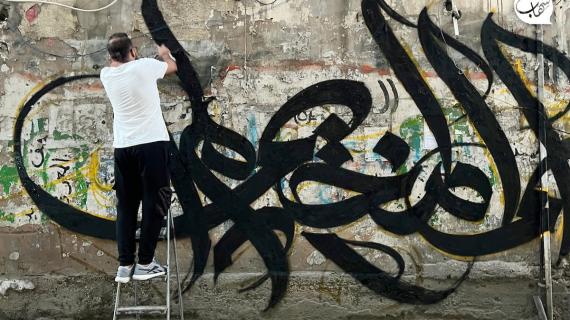 الفنان الفلسطيني بلال خالد يرسم جدارية "باسم المخيم أنا لم أمت واسأل جنين" على جدار في مخيم برج البراجنة في لبنان