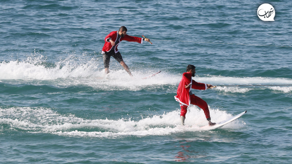 فلسطينيون يرتدون زي "بابا نويل" خلال المشاركة في عرض للتزلج بمناسبة أعياد الميلاد على شاطئ بحر غزة